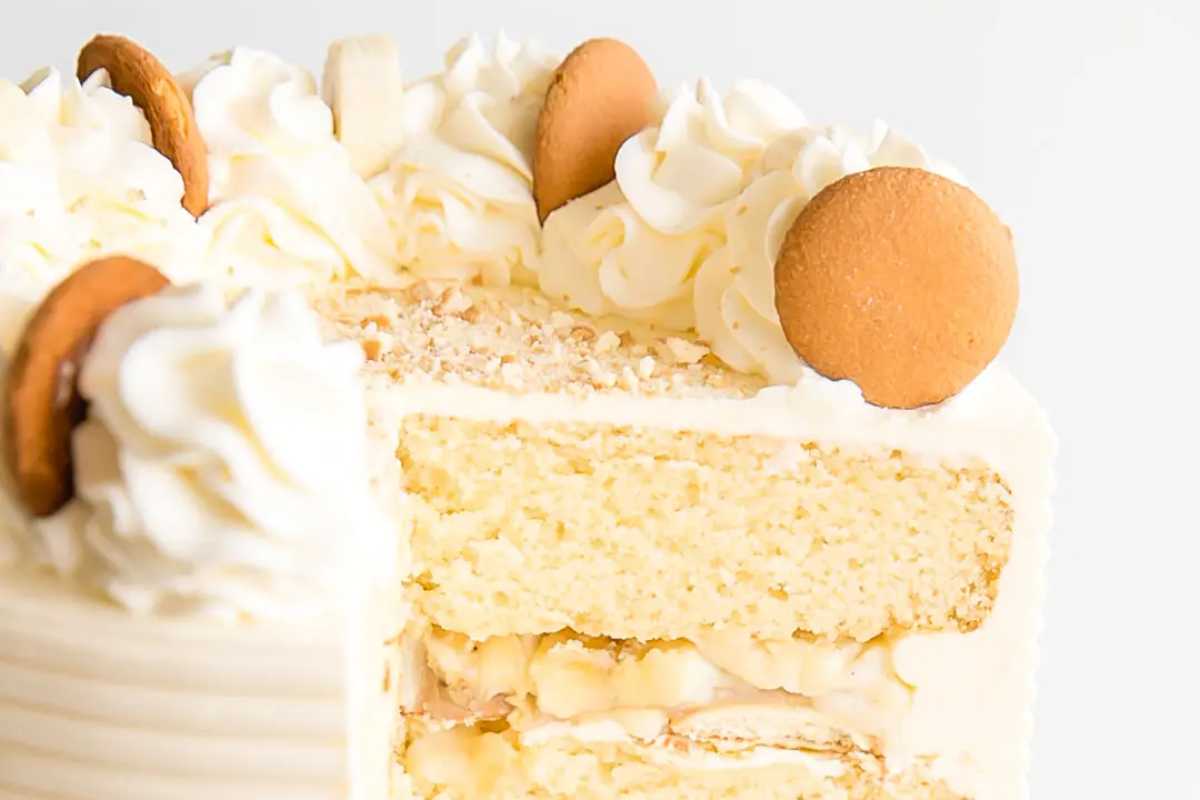 A slice of layered vanilla cake with whipped cream frosting and cookie toppings, displayed on a white background.