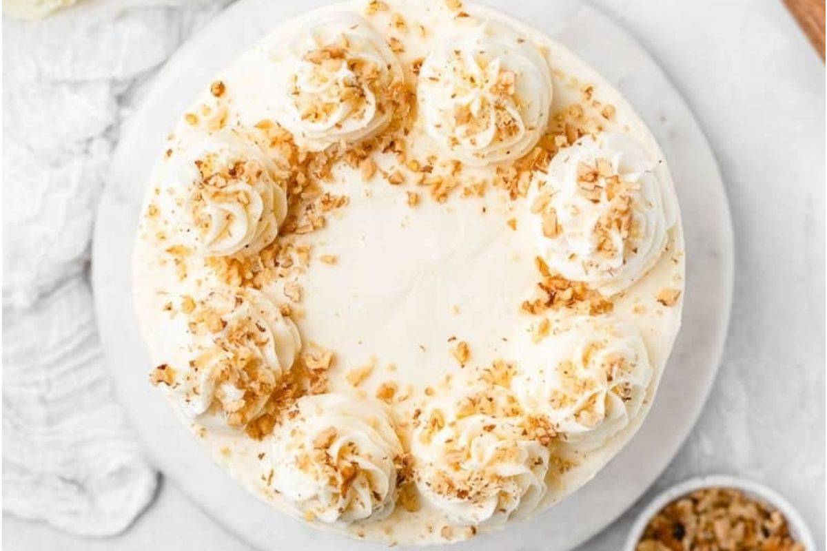 A frosted cake with decorative swirls and sprinkled nuts on top.