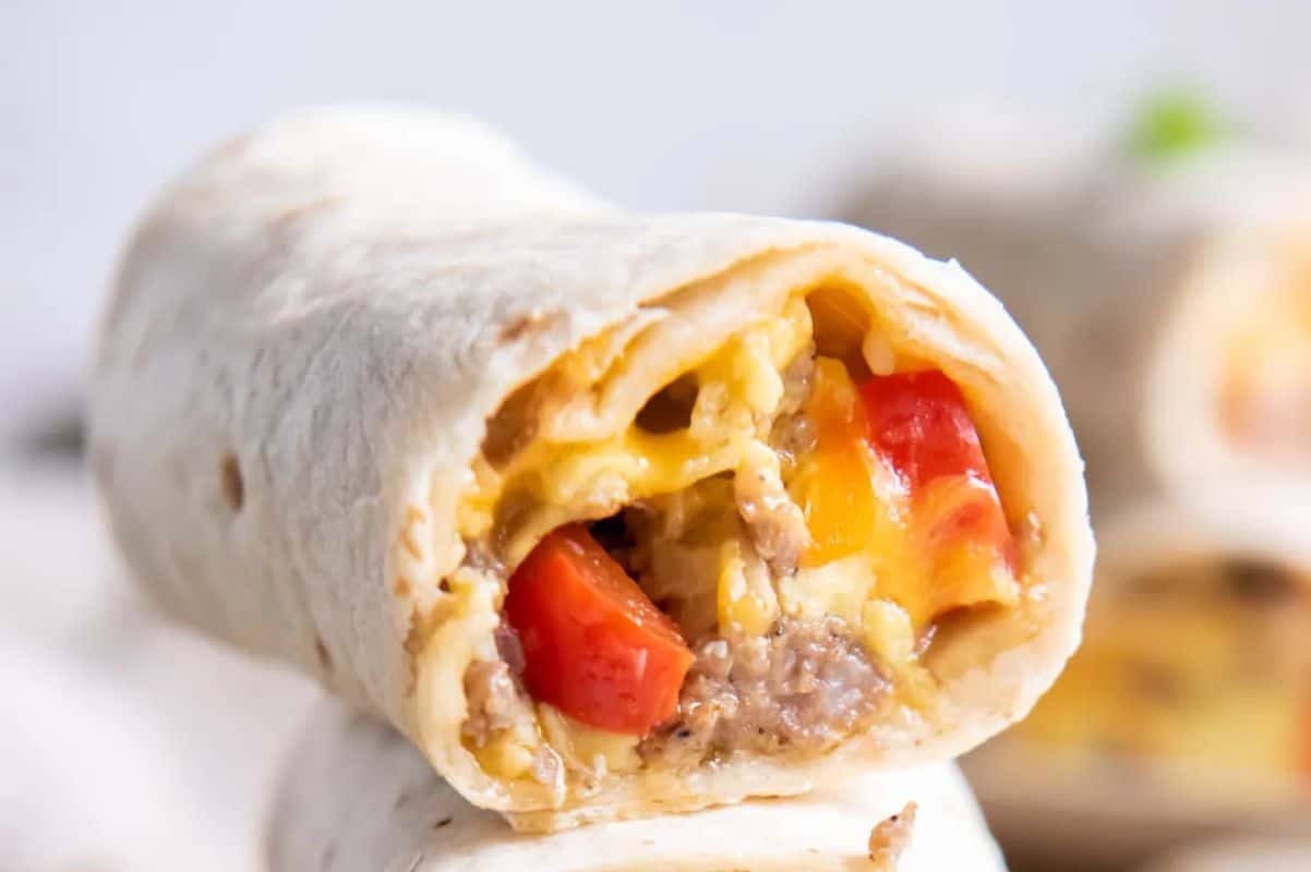 Close-up of a breakfast burrito with visible fillings of scrambled eggs, sausage, and diced vegetables.