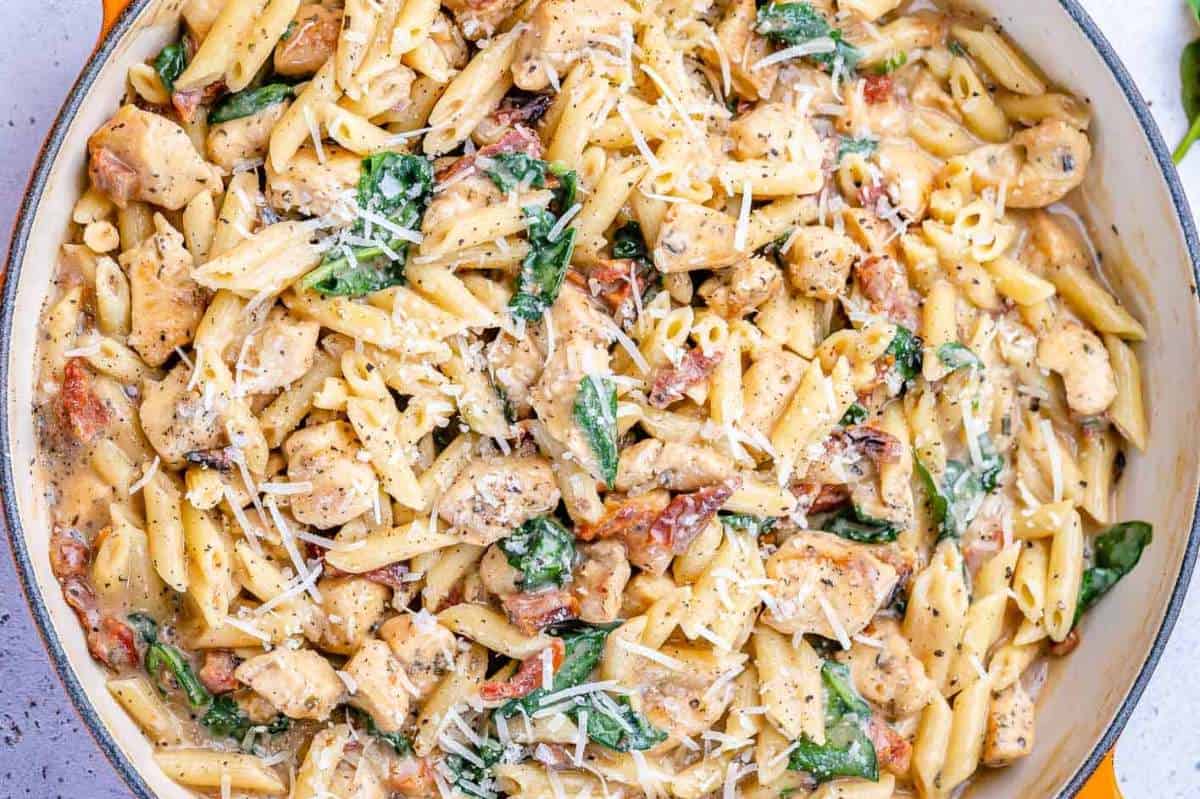 A close-up view of creamy chicken pasta with spinach and sun-dried tomatoes, sprinkled with grated cheese.