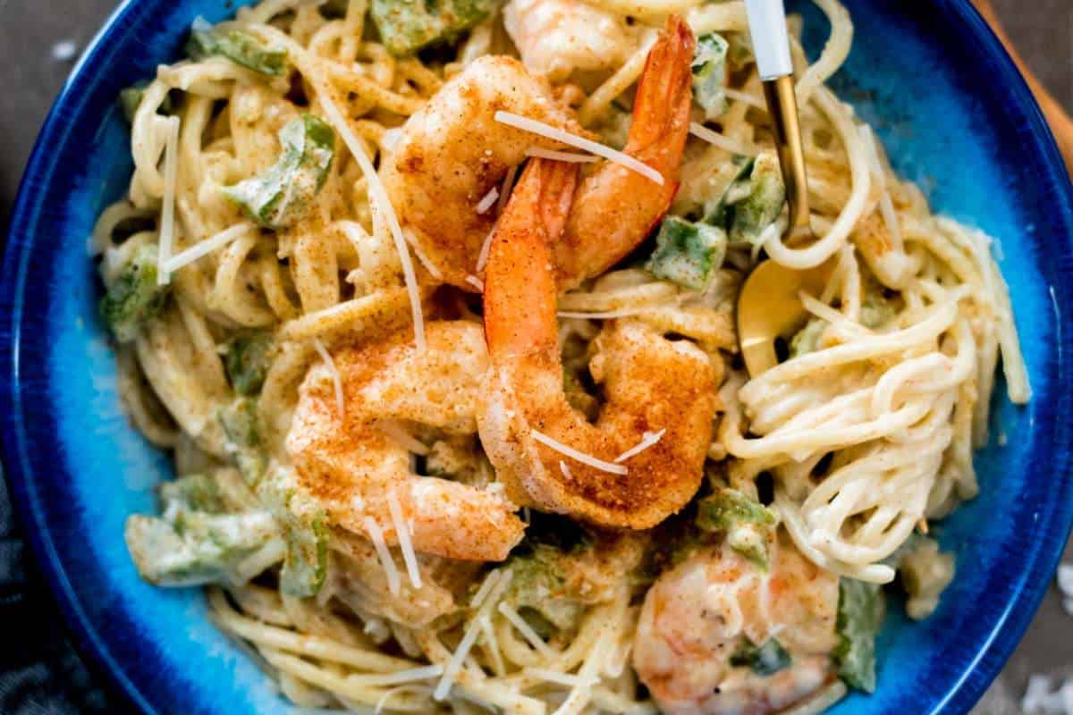 A bowl of creamy pasta with seasoned shrimp and green herbs.