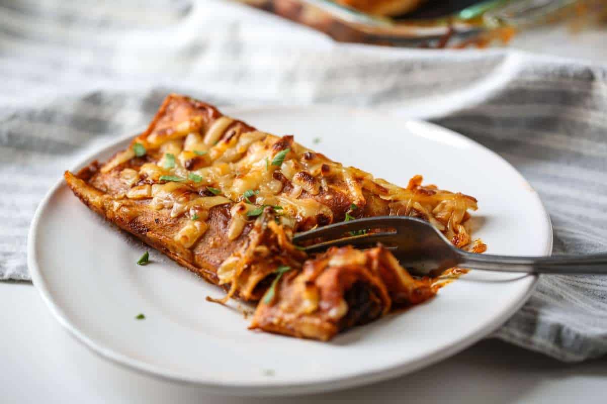 A slice of caramelized onion pizza on a white plate with a fork, garnished with herbs, on a textured tablecloth.