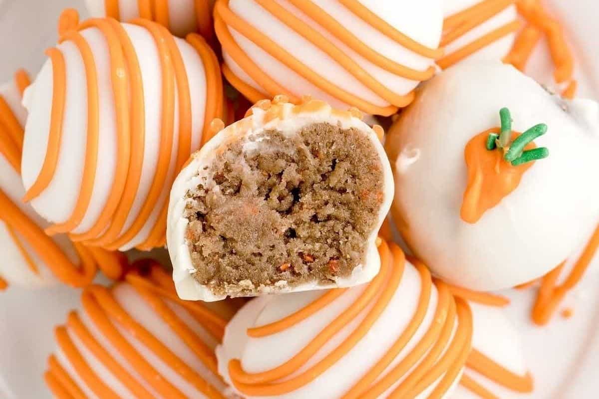 Carrot cake truffles with white chocolate coating and orange drizzle, one truffle is cut in half to show the inside.