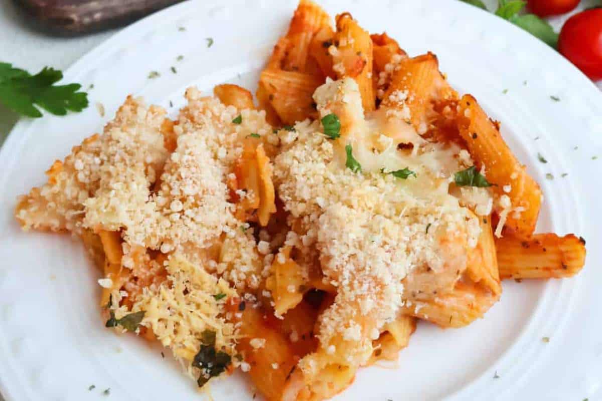 A plate of rigatoni pasta with tomato sauce and sprinkled with grated cheese and herbs.