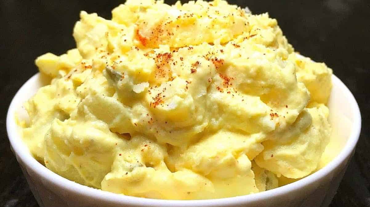 A bowl of creamy potato salad garnished with paprika on top.