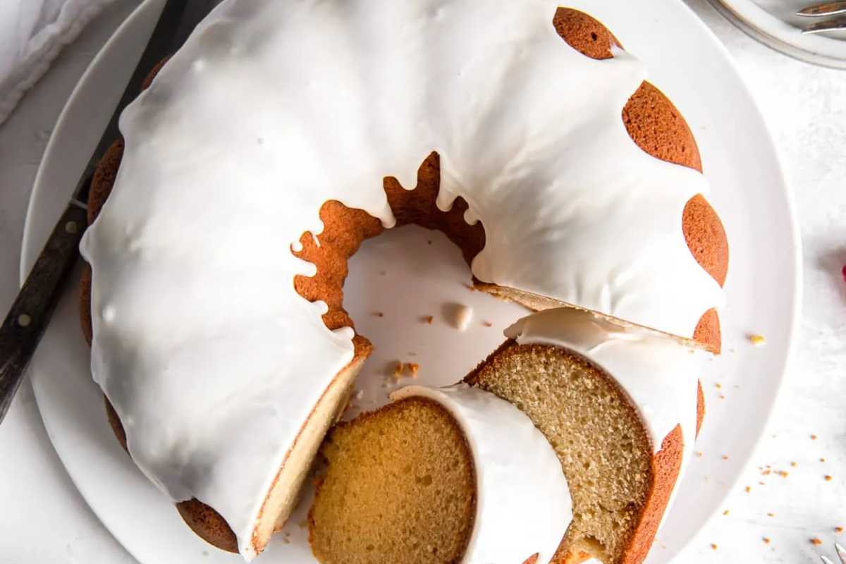 A bundt cake with white icing on a plate, partially sliced.