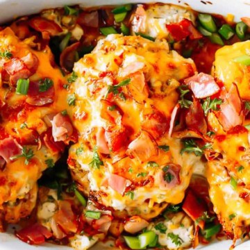 Baked chicken breasts topped with cheese, ham, and herbs in a white casserole dish.
