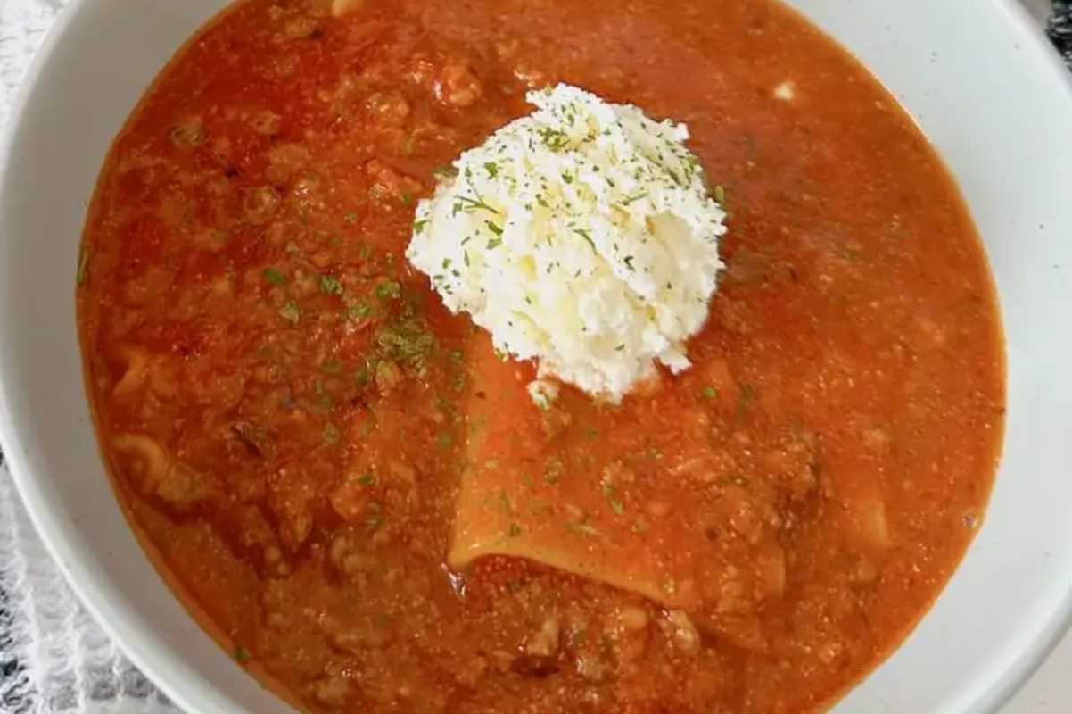 A bowl of tomato soup garnished with a dollop of sour cream and sprinkled herbs.