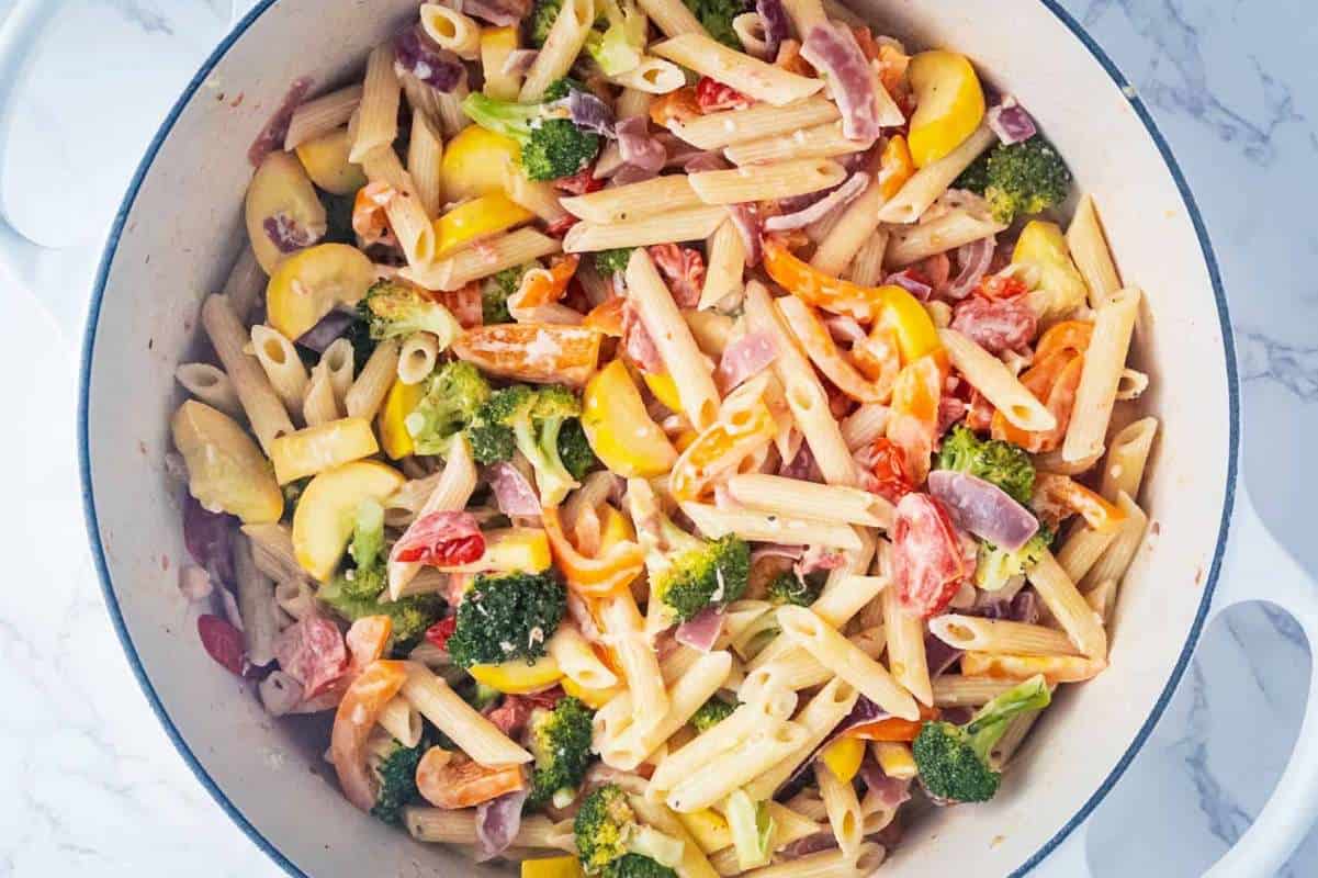A colorful pasta salad with broccoli, tomatoes, and bell peppers in a white serving bowl.