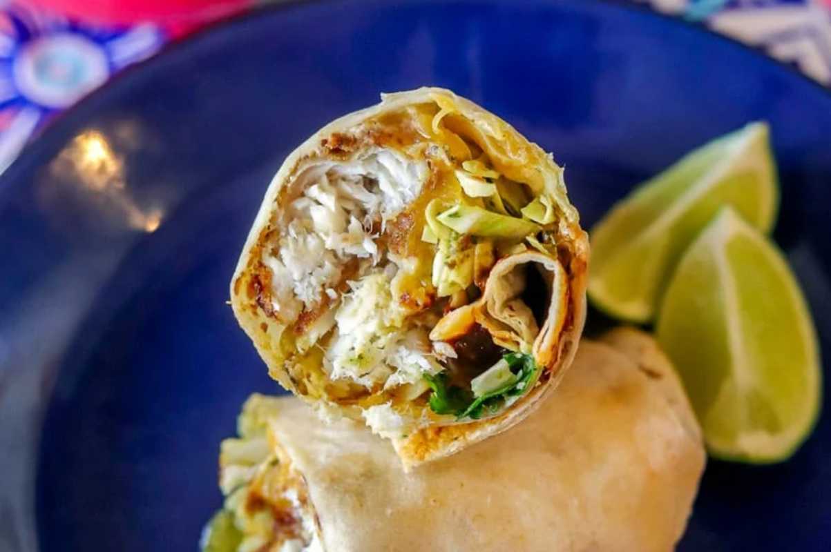 Close-up of a cut burrito with chicken, cheese, and vegetables on a blue plate with lime wedges.