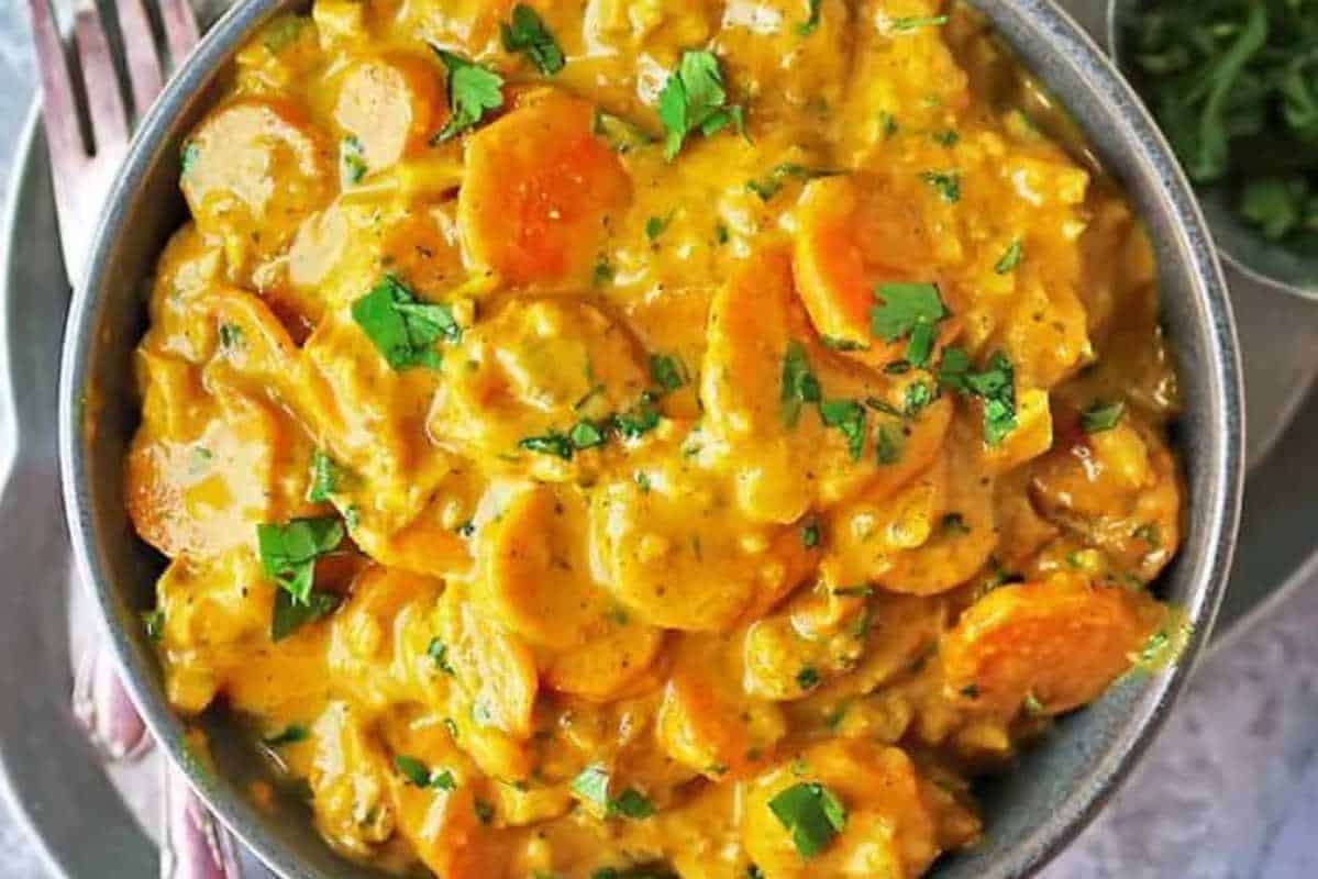 A bowl of creamy vegetable curry garnished with fresh herbs, featuring sliced carrots and potatoes.