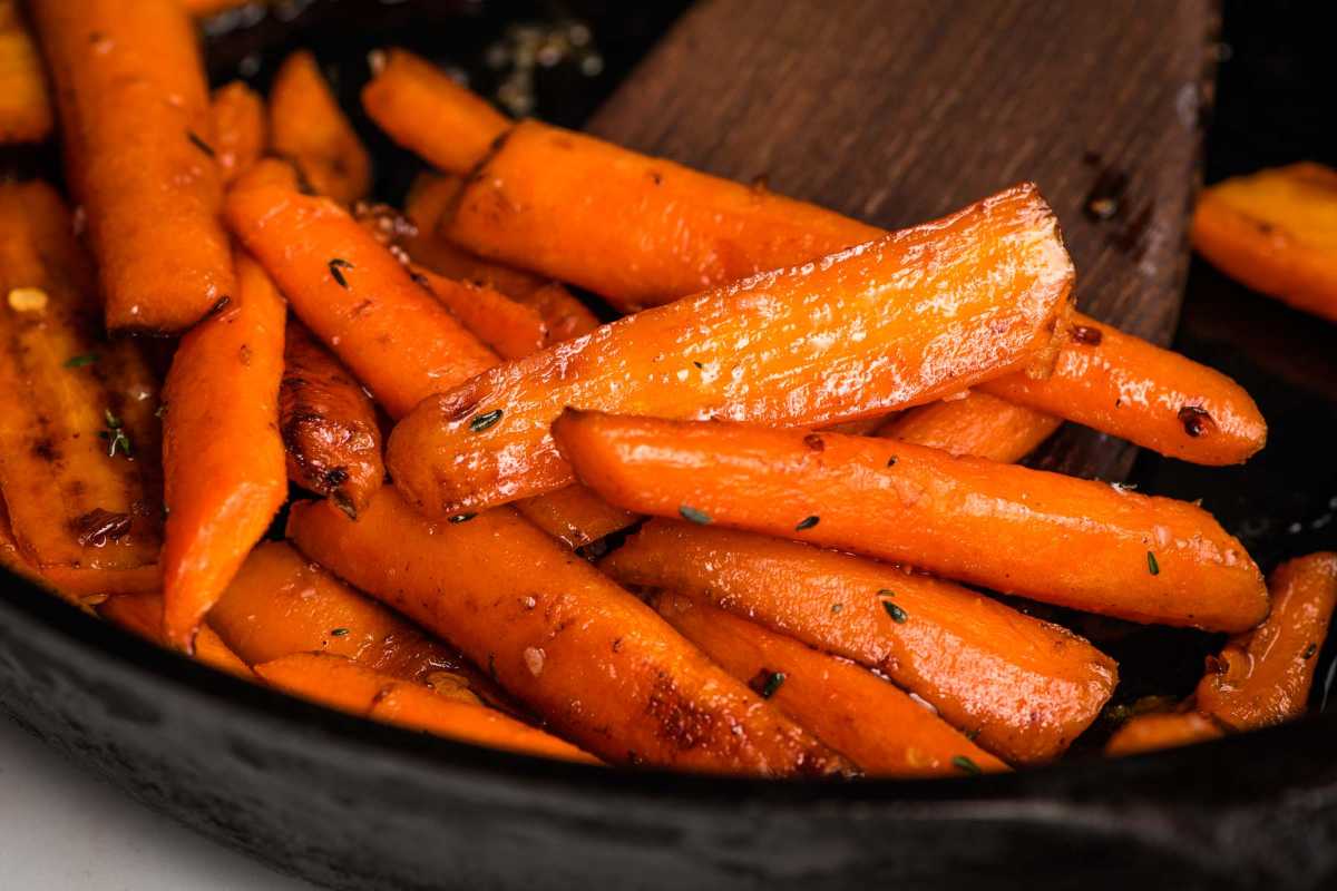 Roasted carrots with herbs in a black bowl, a wooden spoon stirring.