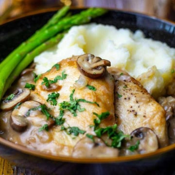A plate of chicken with mushroom sauce, mashed potatoes, and green asparagus.