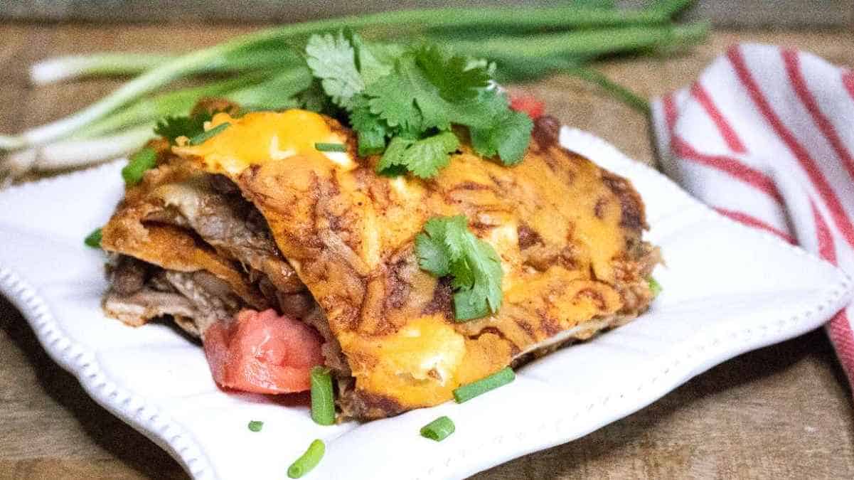 A serving of enchiladas garnished with cilantro and green onions on a white plate, with fresh ingredients in the background.