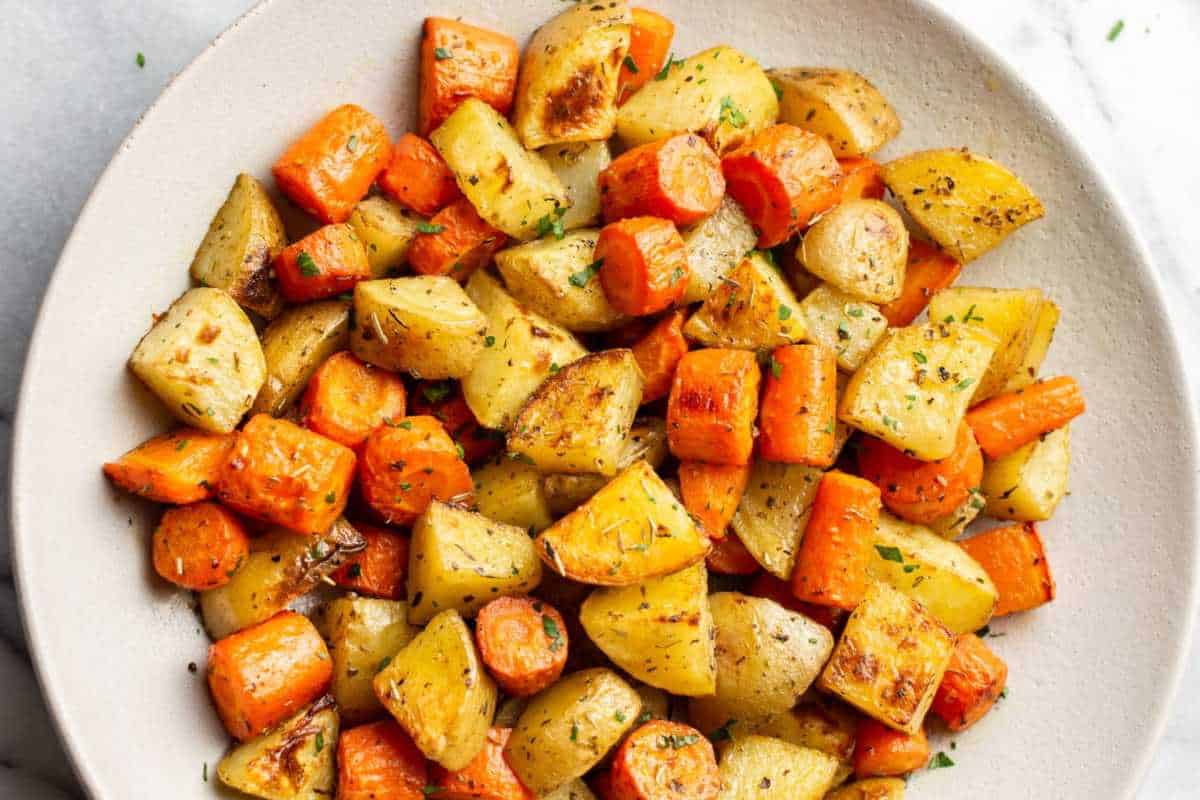 A plate of roasted carrots and potatoes garnished with herbs.