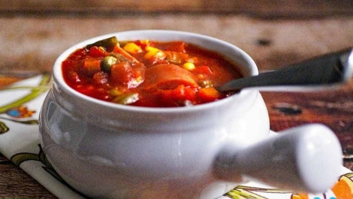 A bowl of vegetable soup with a spoon on a wooden table.