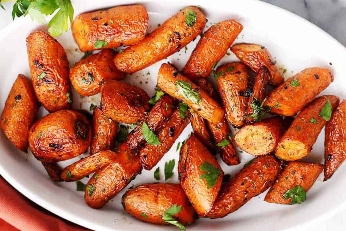 Roasted carrots garnished with parsley in a white dish.