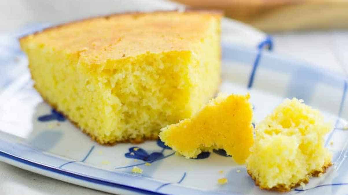 A slice of yellow cornbread on a patterned plate with a piece broken off.
