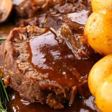 Braised beef brisket with a rich gravy, accompanied by roasted potatoes and a sprig of rosemary.