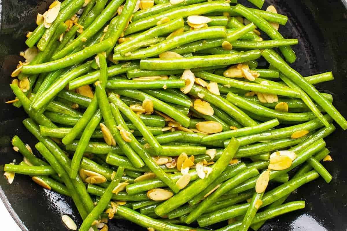 Sautéed green beans with sliced garlic in a black skillet.