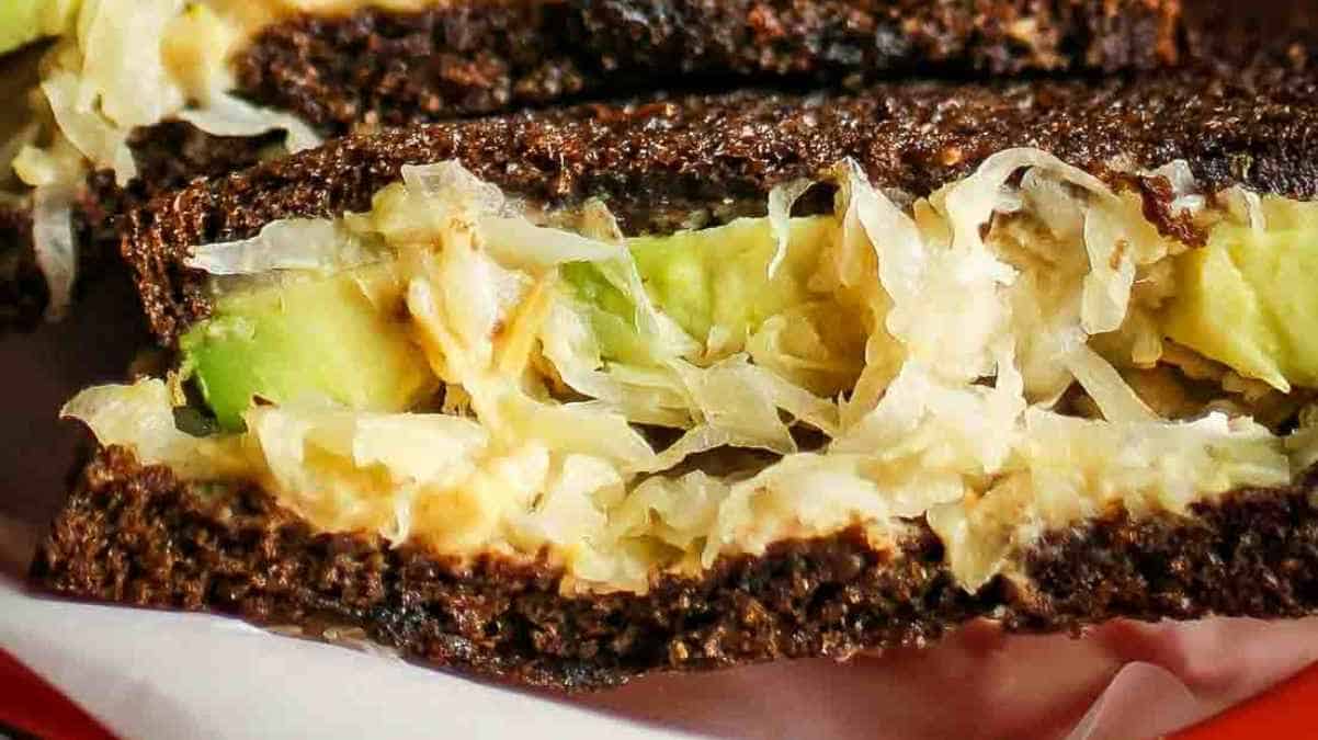 A close-up of a sandwich with rye bread and a filling that appears to include avocado and shredded cheese.