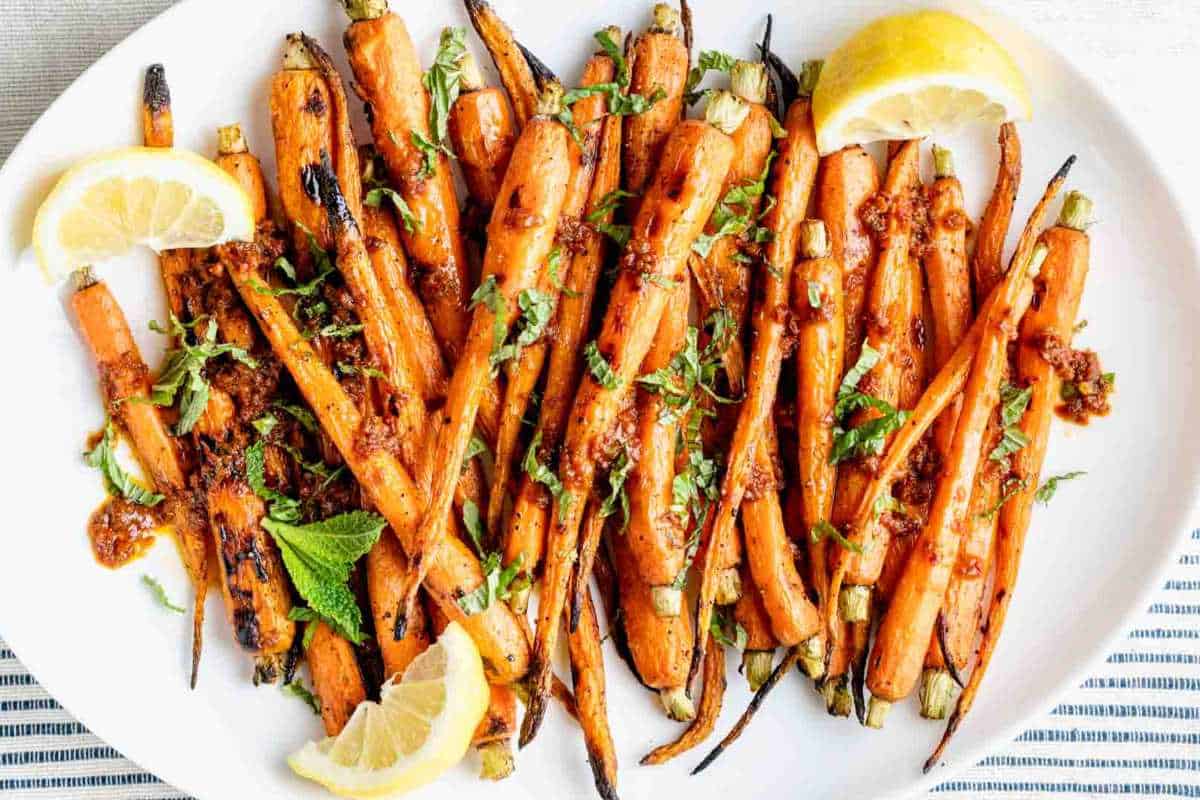 A plate of roasted carrots garnished with lemon slices and fresh herbs, served on a striped tablecloth.