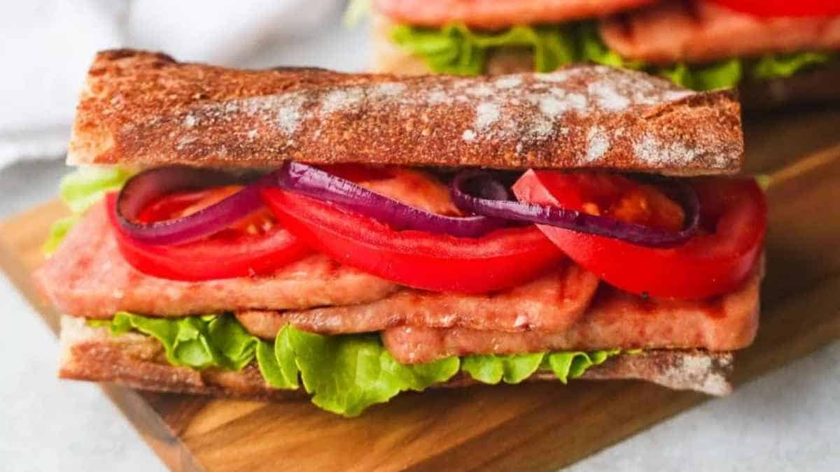 A sandwich with lettuce, tomato, onion, and meat on a wooden board.