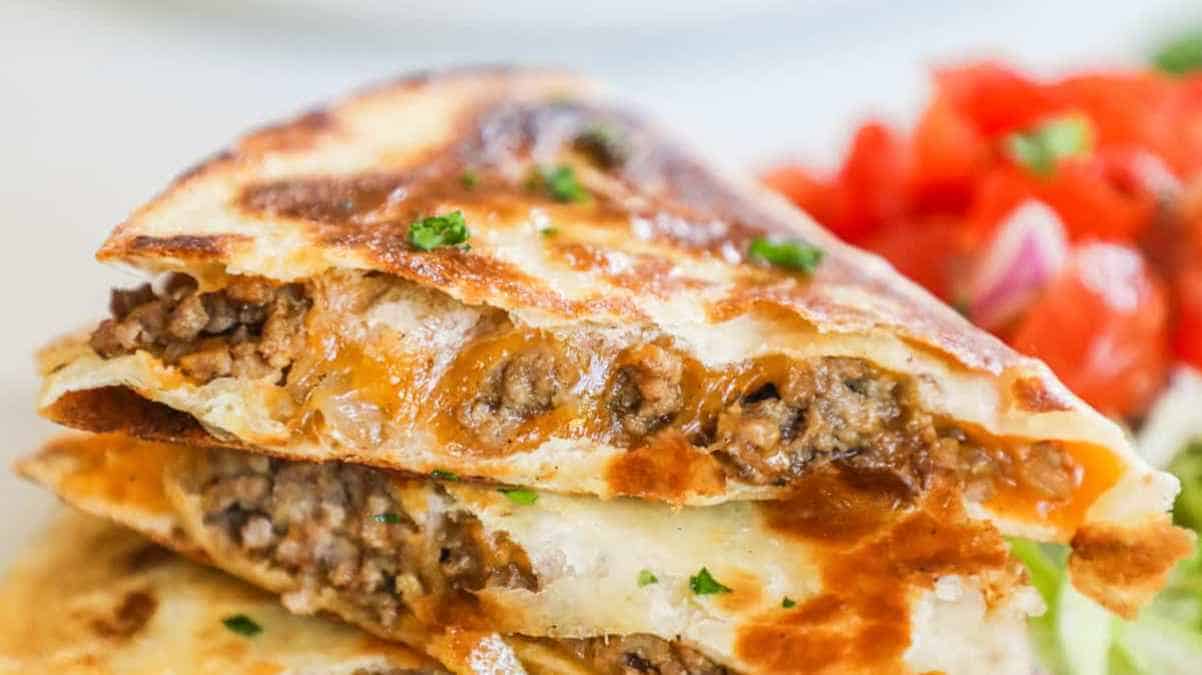 A close-up of a sliced quesadilla filled with seasoned ground beef and melted cheese, served with a side of diced tomatoes.