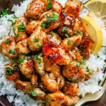Grilled chicken pieces over white rice garnished with herbs and a lemon wedge on the side.