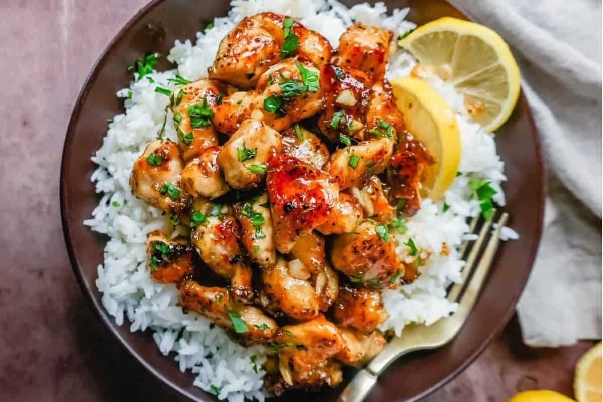 Grilled chicken pieces over white rice garnished with herbs and a lemon wedge on the side.