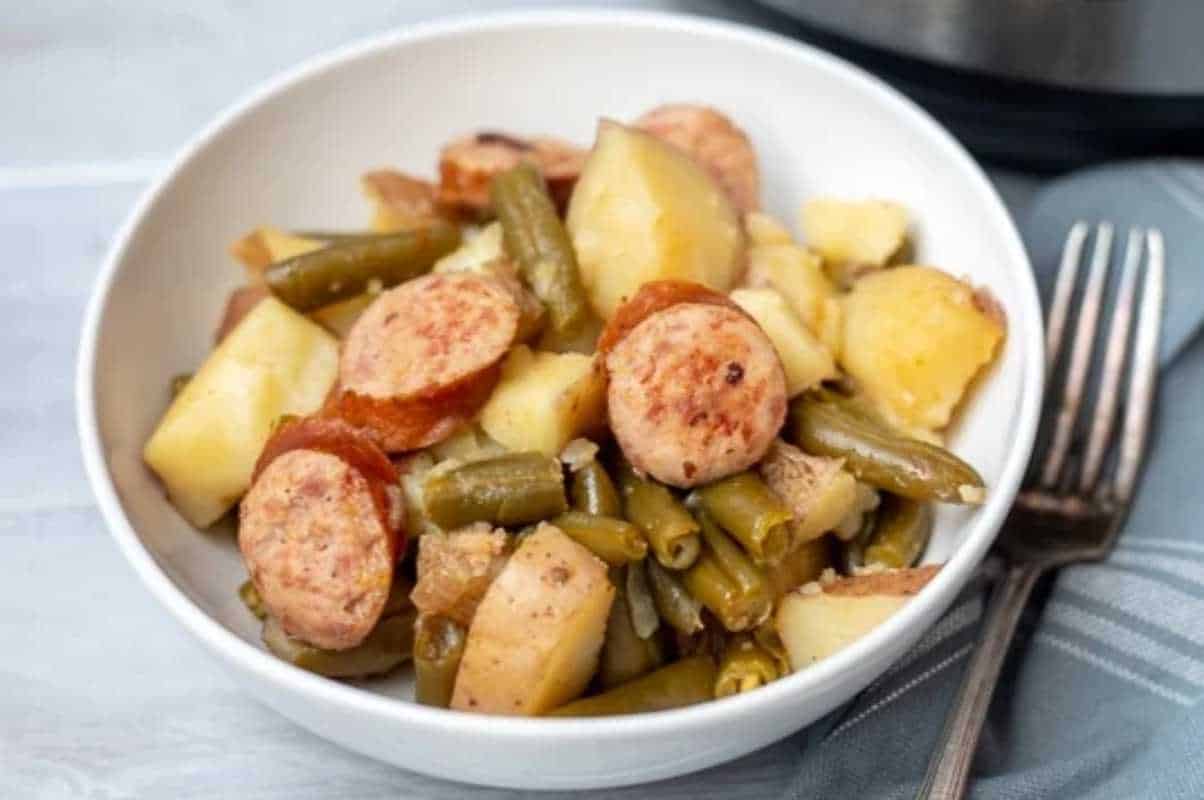 A bowl of stew with sliced sausages, potatoes, and green beans.