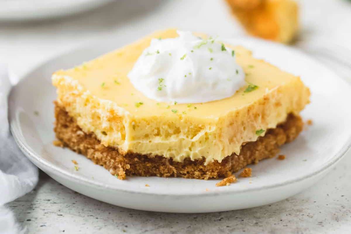 A slice of key lime pie with a creamy topping and lime zest on a white plate, accompanied by a dessert fork.