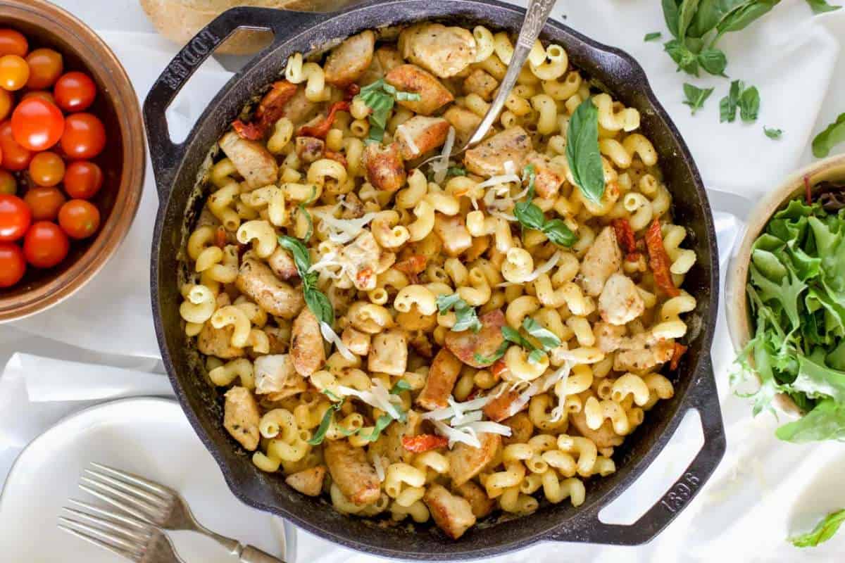 A skillet with pasta, chicken, and vegetables, topped with shredded cheese.