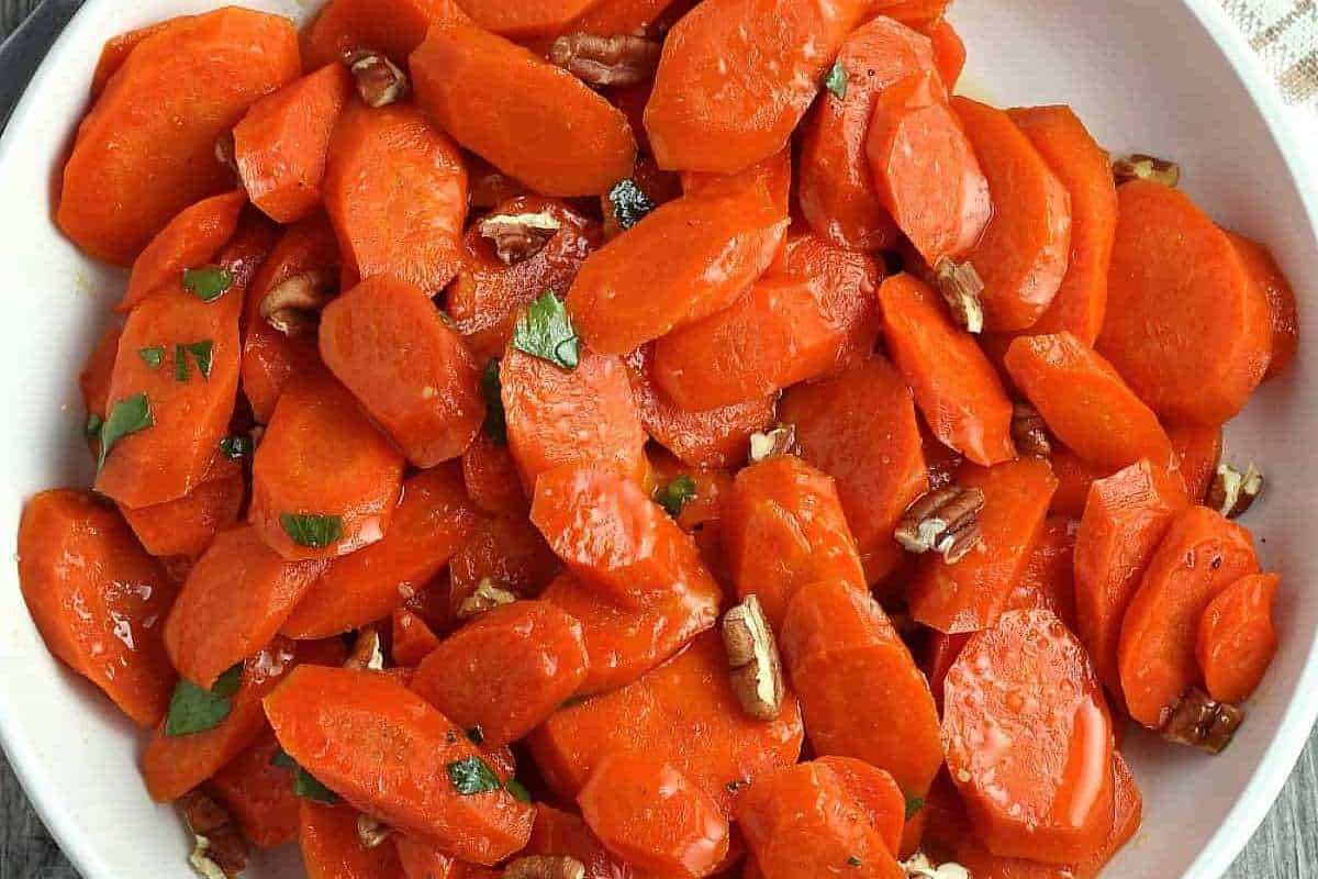 A bowl of glazed carrots topped with pecans and garnished with fresh herbs.
