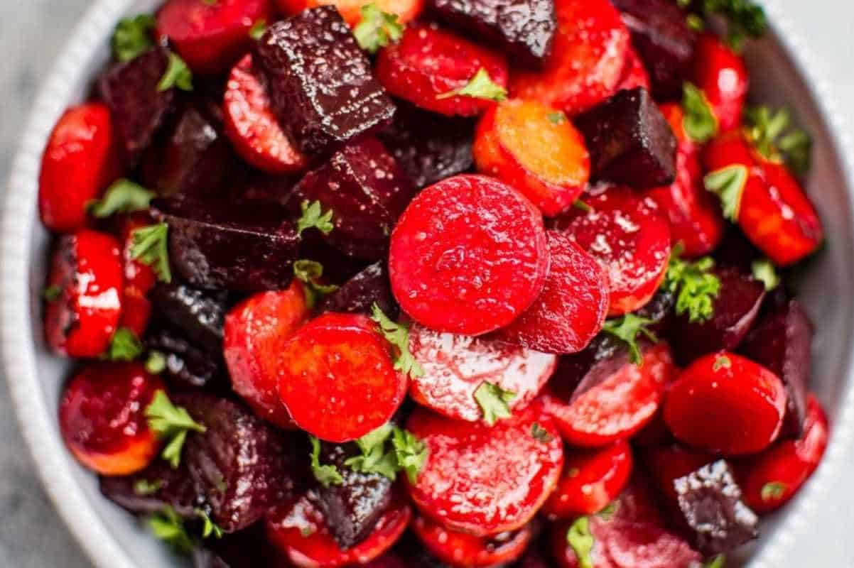 A colorful bowl of roasted beet and carrot salad, garnished with fresh parsley.