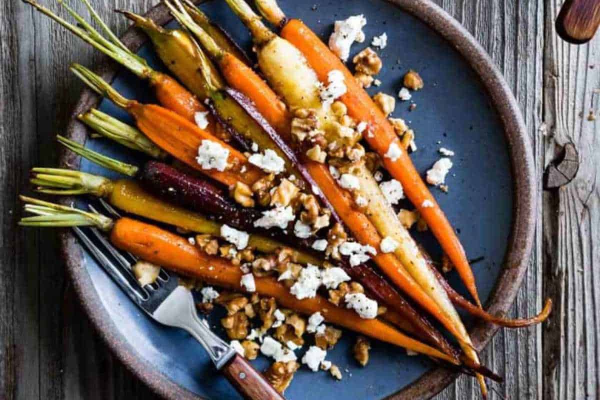 Roasted carrots with assorted colors served on a blue plate, topped with crumbled cheese and walnuts.