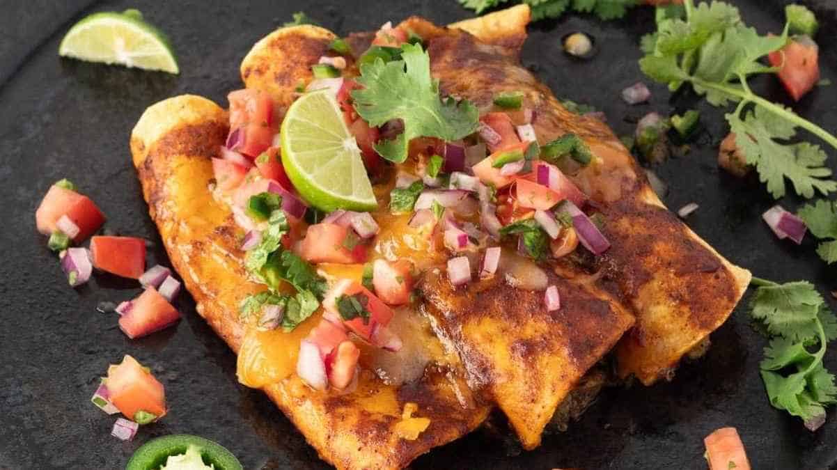 Plate of enchiladas topped with salsa, lime slices, and fresh cilantro on a dark surface.