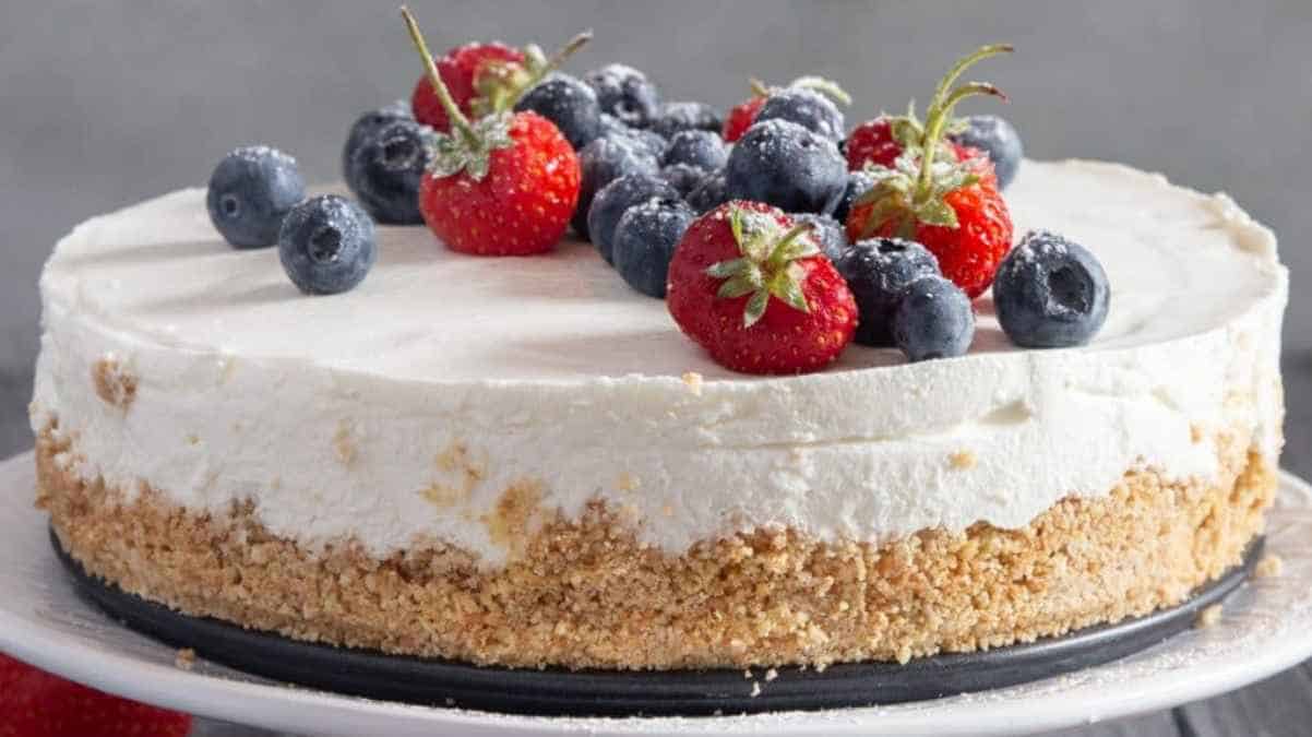 A creamy cheesecake topped with fresh strawberries and blueberries on a crumbly crust, presented on a white plate.