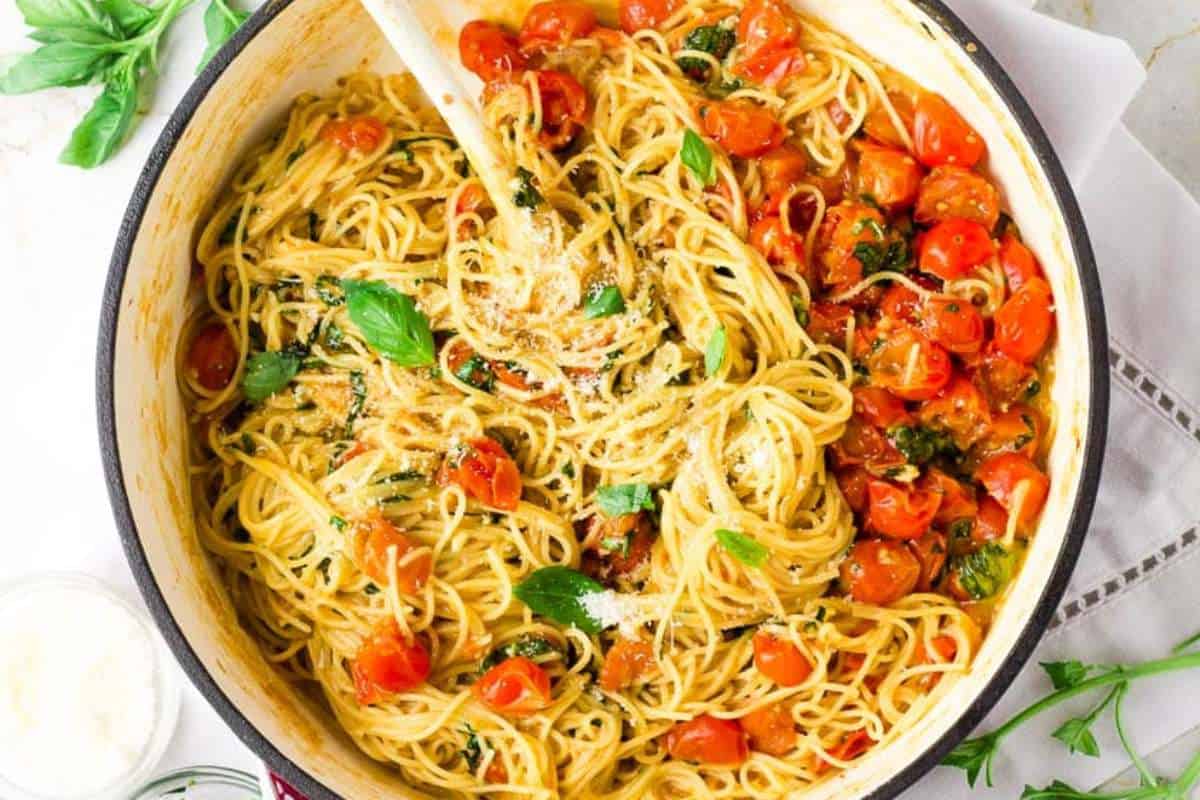 A pot of spaghetti with cherry tomatoes, basil, and grated cheese.