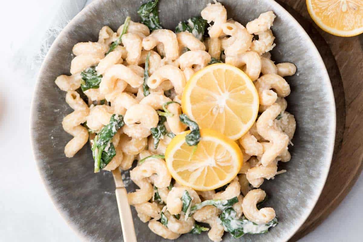 A bowl of pasta with leafy greens and lemon slices.