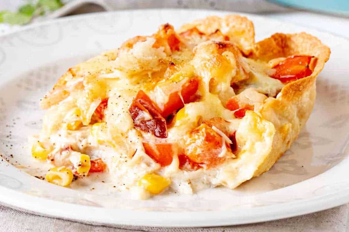 A slice of tomato and corn galette on a white plate, sprinkled with black pepper.