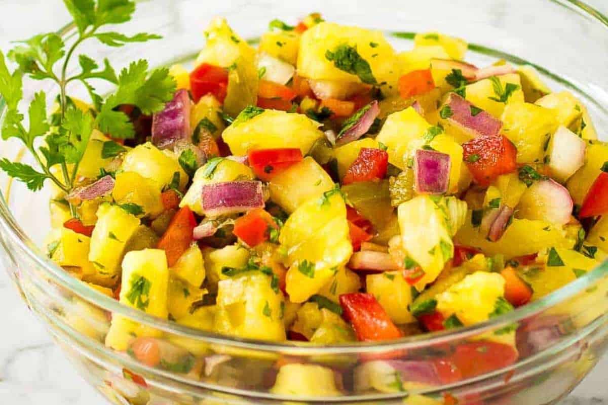 A bowl of fresh pineapple salsa with diced red onions, tomatoes, and cilantro, garnished with a parsley sprig.