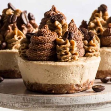 Three coffee-flavored mini cheesecakes garnished with coffee beans and piped cream on a white stand.