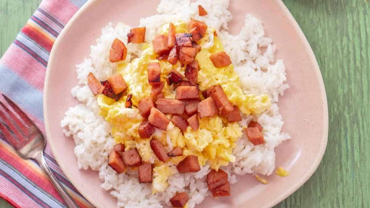 A plate of scrambled eggs and diced ham over white rice.