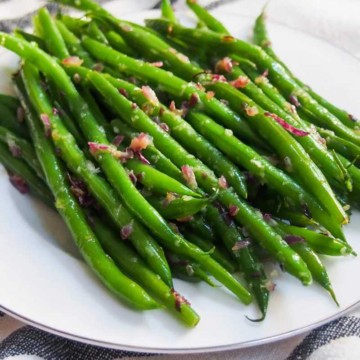 A plate of cooked green beans topped with diced bacon, served on a striped cloth.