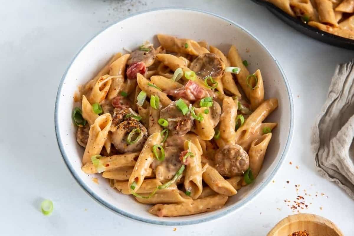 A bowl of creamy pasta with sliced mushrooms and garnished with spring onions.