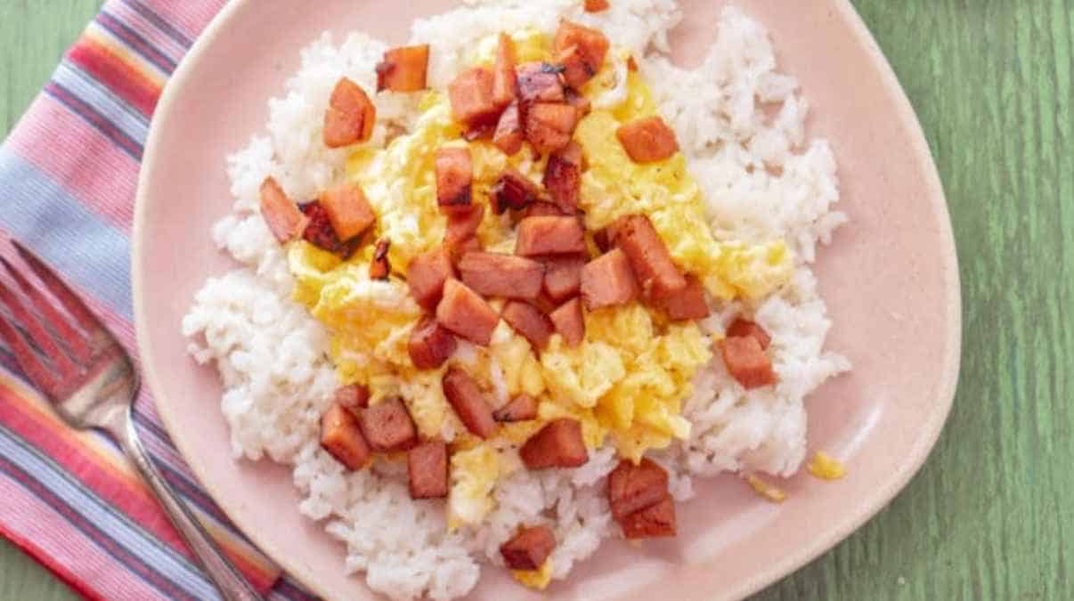 A plate of white rice topped with scrambled eggs and diced ham.