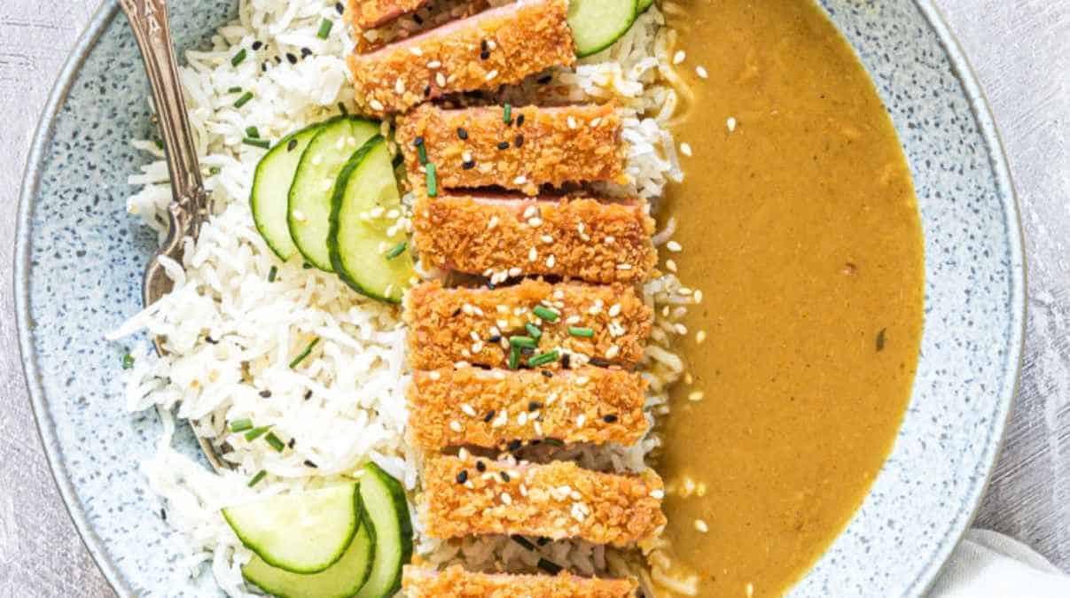 Breaded and sliced meat served with rice, cucumber, and a side of sauce.