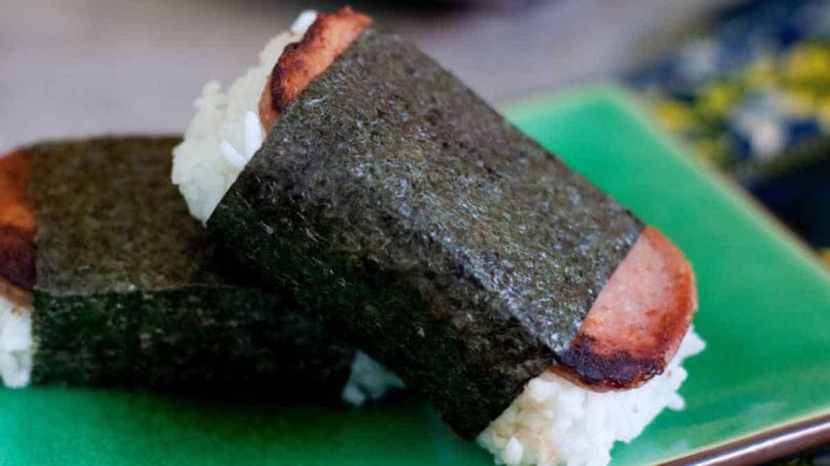 A piece of spam musubi on a green plate.