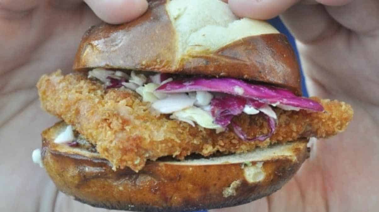 A person holding a crispy chicken sandwich with coleslaw on a pretzel bun.